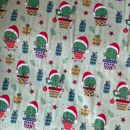 Christmas-themed fabric with cacti wearing Santa hats and presents on a green background