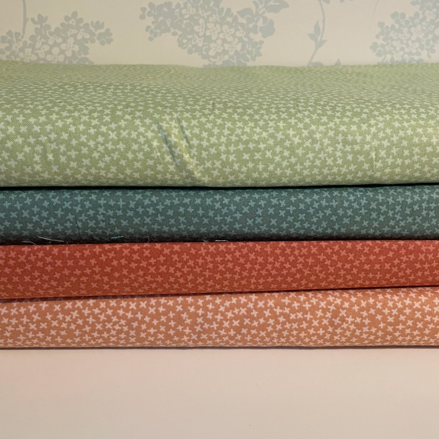 Stack of fabric swatches in green, blue, red, and brown with subtle patterns on a neutral background.