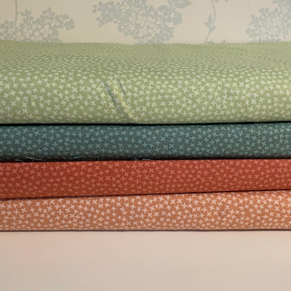 Stack of fabric swatches in green, blue, red, and brown with subtle patterns on a neutral background.