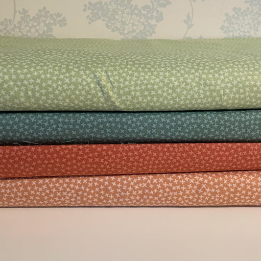 Stack of fabric swatches in green, blue, red, and brown with subtle patterns on a neutral background.